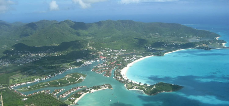 Aerial view of a lush coastal town with blue waters, white sand beaches, and green hills.